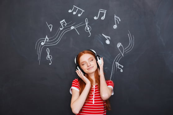 Relaxed smiling beautiful young woman listening to music in headphones over chalkboard background